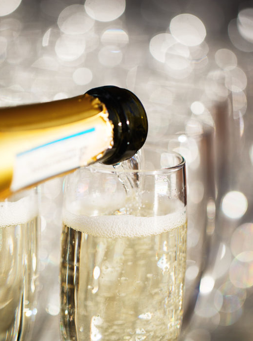 close up of a bottle pouring champagne into glasses with blurred background