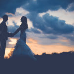 Bride and groom hold hands with dusk sky in background