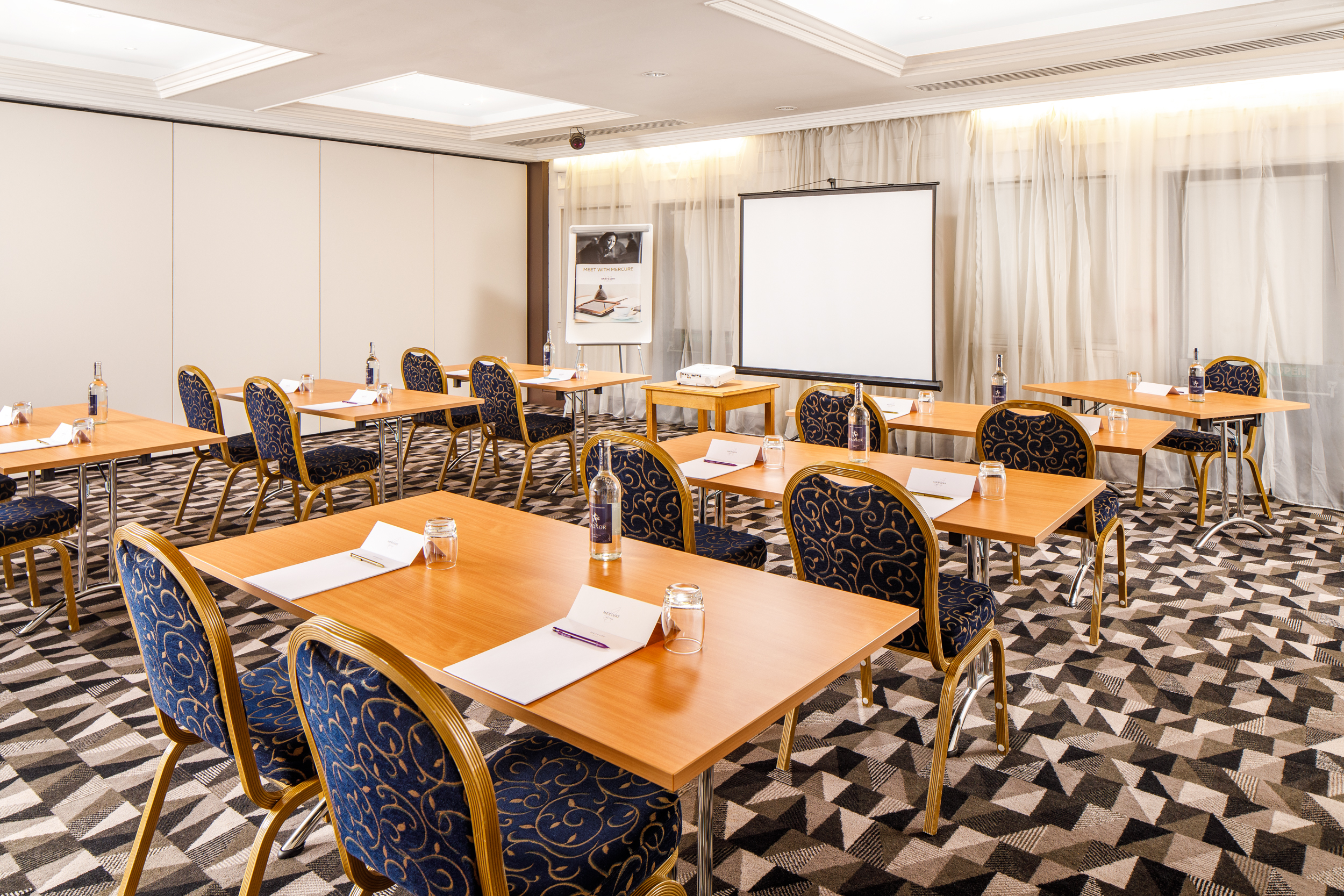 Lakeside 2 Long table seating 18 in The Congress Room at mercure gloucester bowden hall hotel ready for a meeting, with notepads, bottles of water and bowls of apples on the table