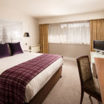 Classic double bedroom with mural behind bed, purple velvet cushions and throw, desk tv