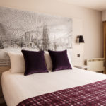 Classic double bedroom with mural behind bed, purple velvet cushions and throw