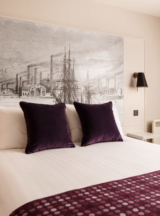 Classic double bedroom with mural behind bed, purple velvet cushions and throw