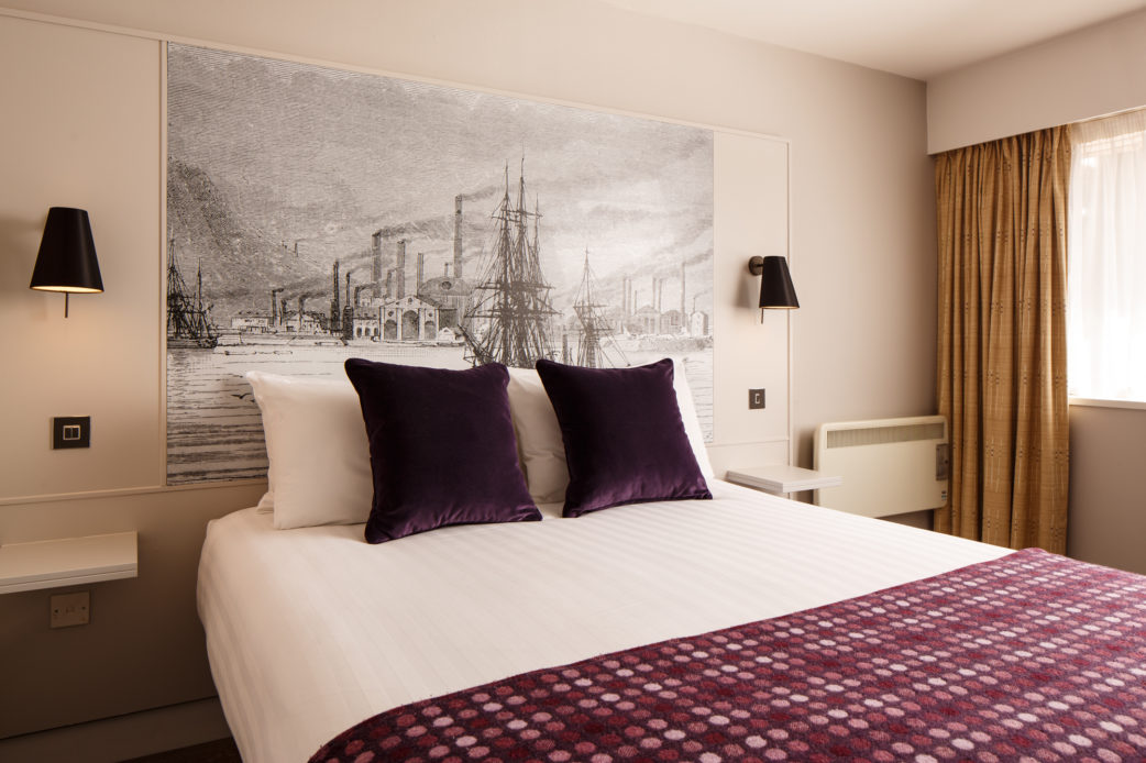 mercure-swansea-hotel-classic-double-room-04-lr-280415 Classic double bedroom with mural behind bed, purple velvet cushions and throw